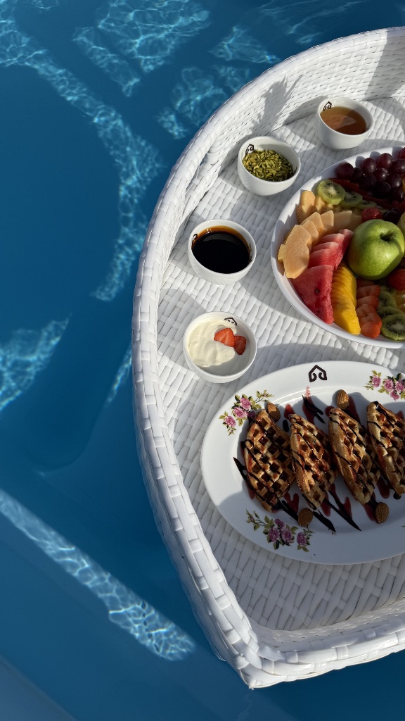 A breakfast tray floating in the pool — fruit, waffles, yoghurt, honey and dates